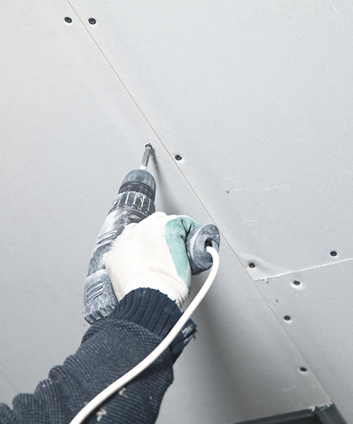contractor hand with glove and drill installing new drywall at ceiling kinnelon nj